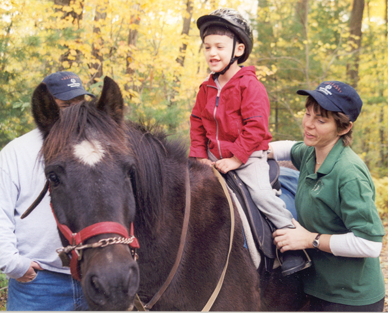 Un bimbo assistito sul cavallo per la pet therapy